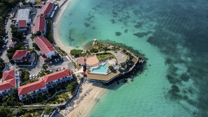 Vue aérienne d’un complexe hôtelier doté d’une plage, d’une piscine et de plusieurs bâtiments aux toits rouges.