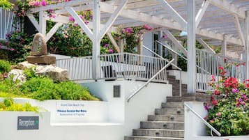 Ein Gebäude mit einer Treppe zu einem überdachten Bereich mit einer Pergola. Ein Schild trägt die Aufschriften "Grand Case Beach Club" und "Entschuldigen Sie die Bauschaft, Renovierung läuft.".