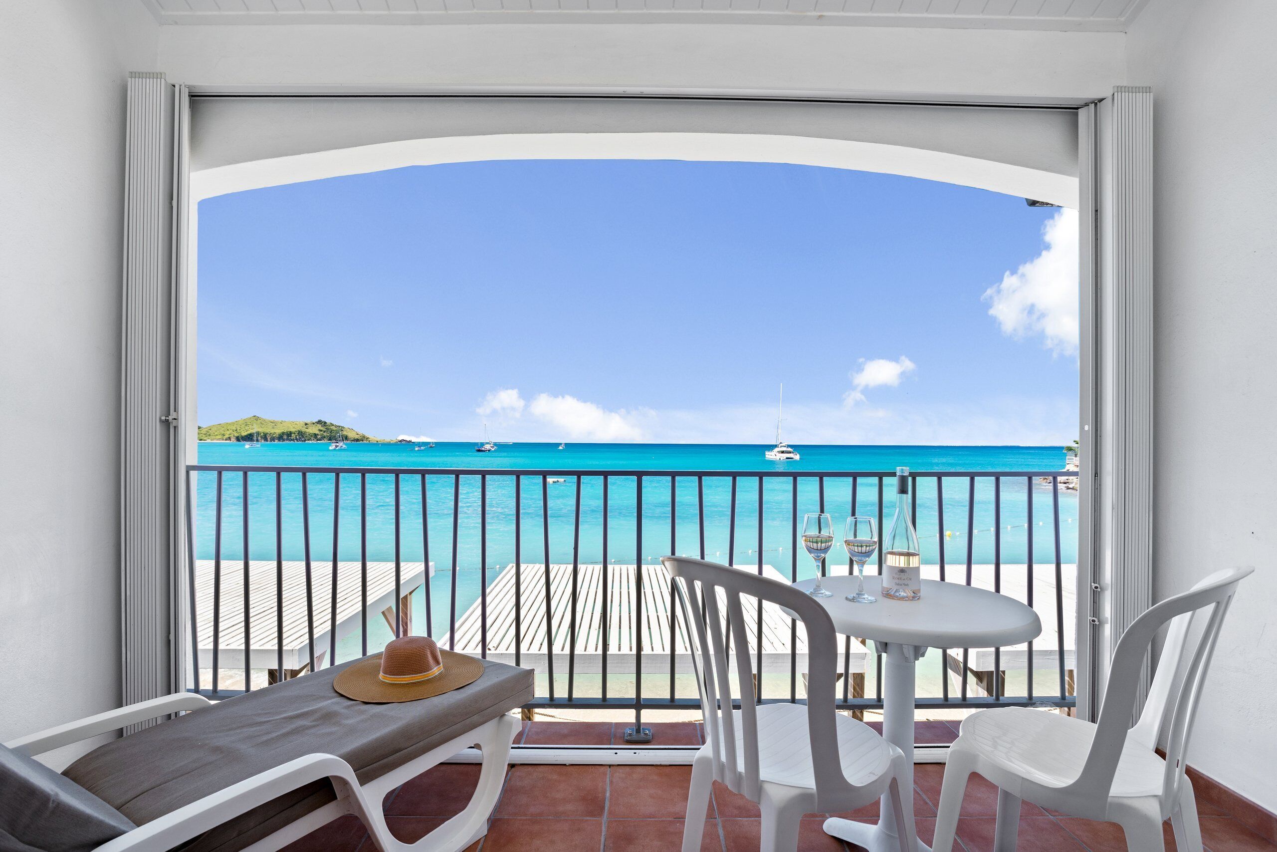 A balcony with a view of the ocean, a table with chairs, and a hat on the bench.