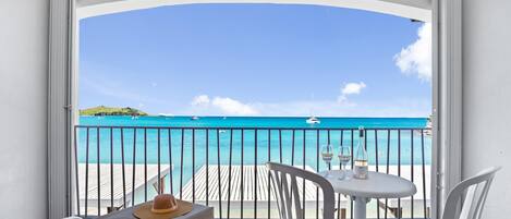 A balcony with a view of the ocean, a table with chairs, and a hat on the bench.