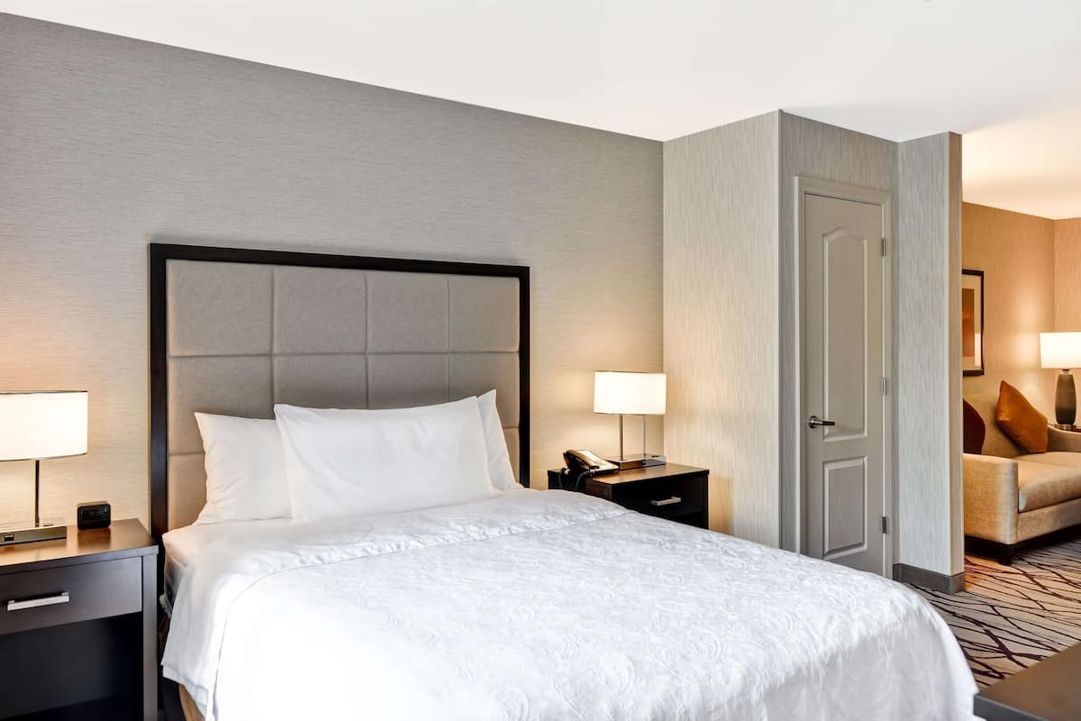Une chambre d’hôtel avec un lit, des tables de chevet, une commode, une lampe, une chaise et une porte.