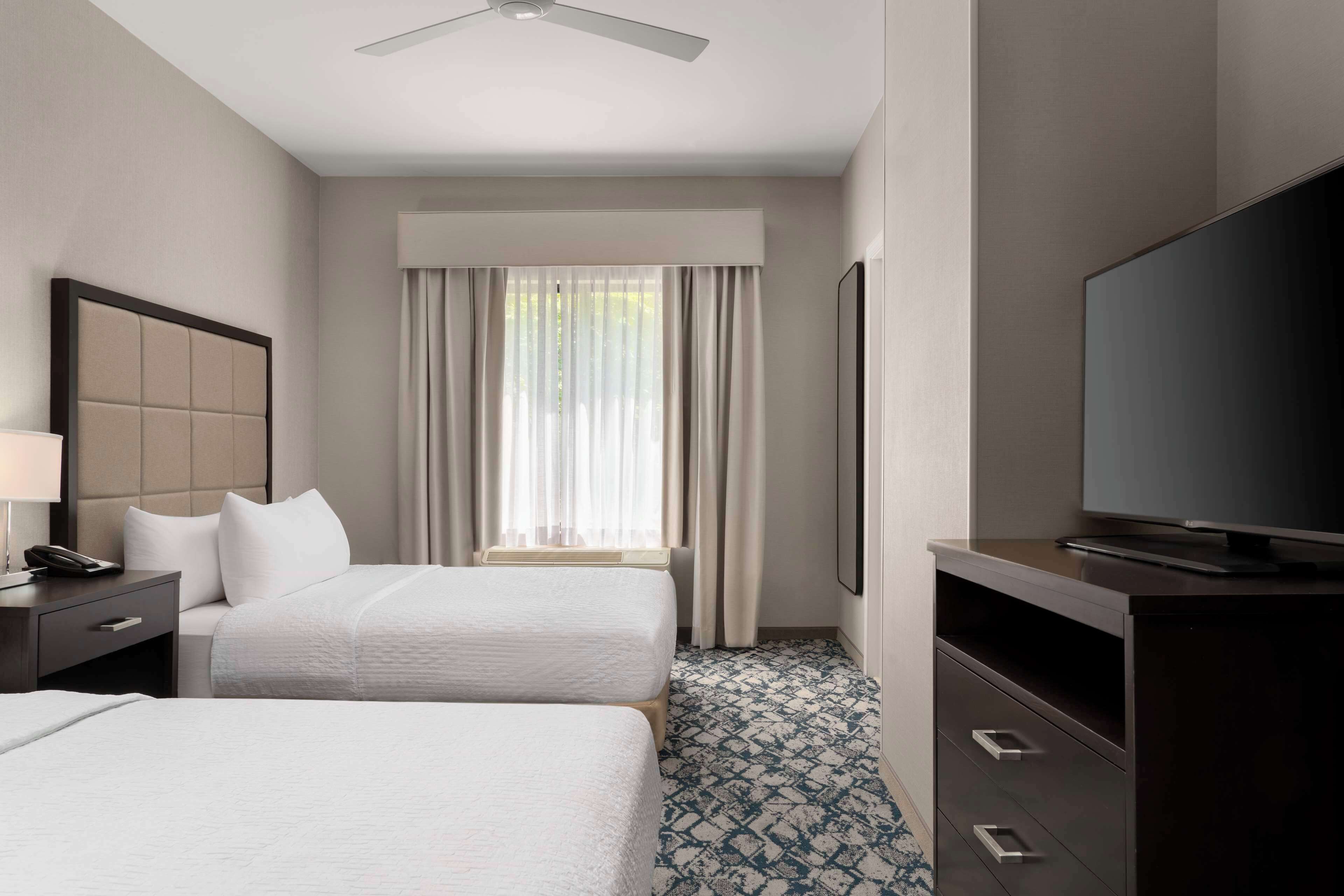Habitación de hotel con dos camas, un televisor, un escritorio con lámpara y una ventana con cortinas.