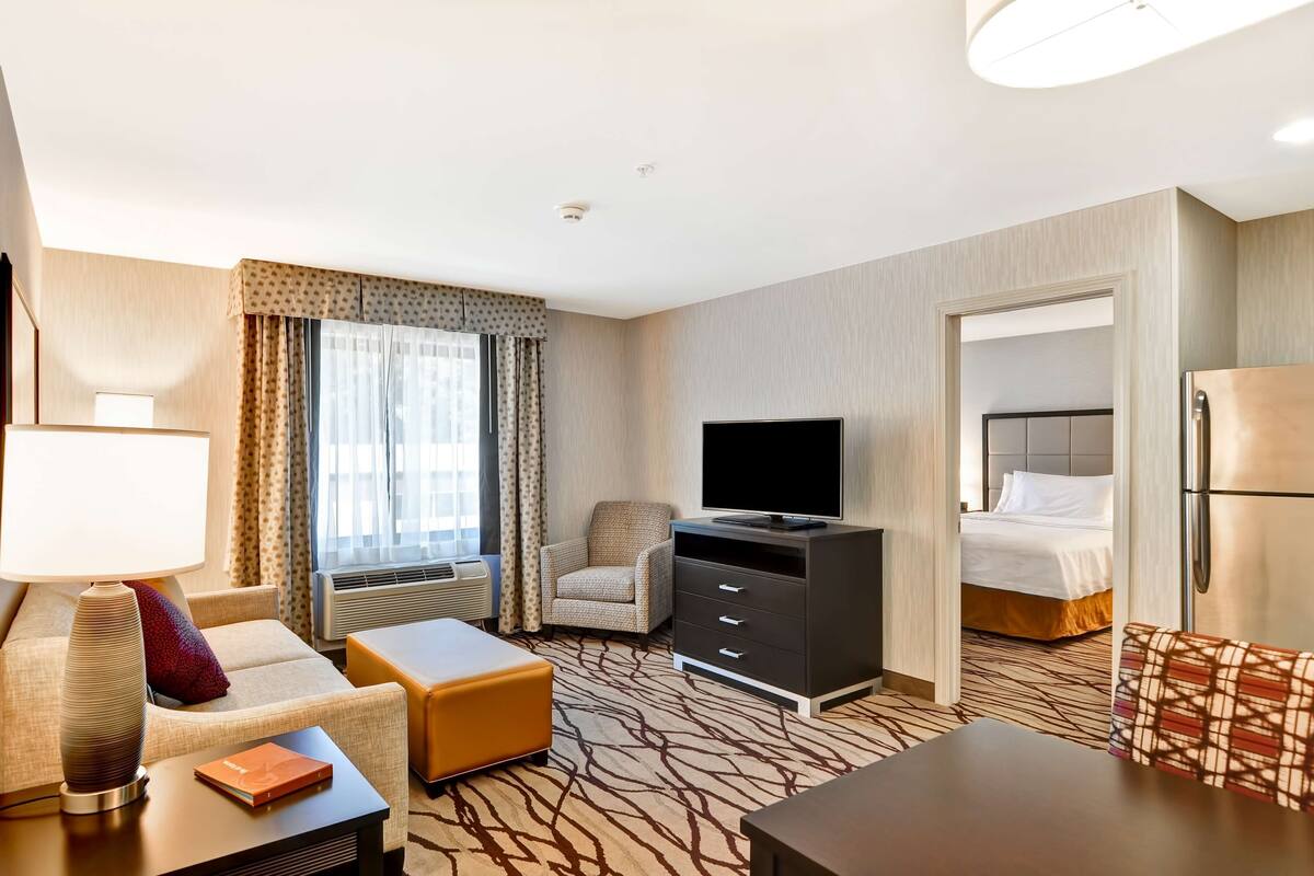 Een hotelkamer met een bank, fauteuil, televisie, dressoir en een bed met hoofdeinde.