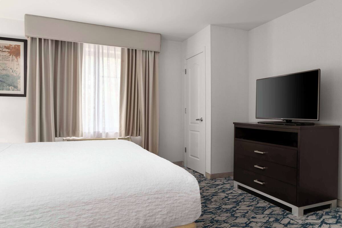 Een hotelkamer met een bed, een televisie op een dressoir, een deur en een raam met gordijnen.