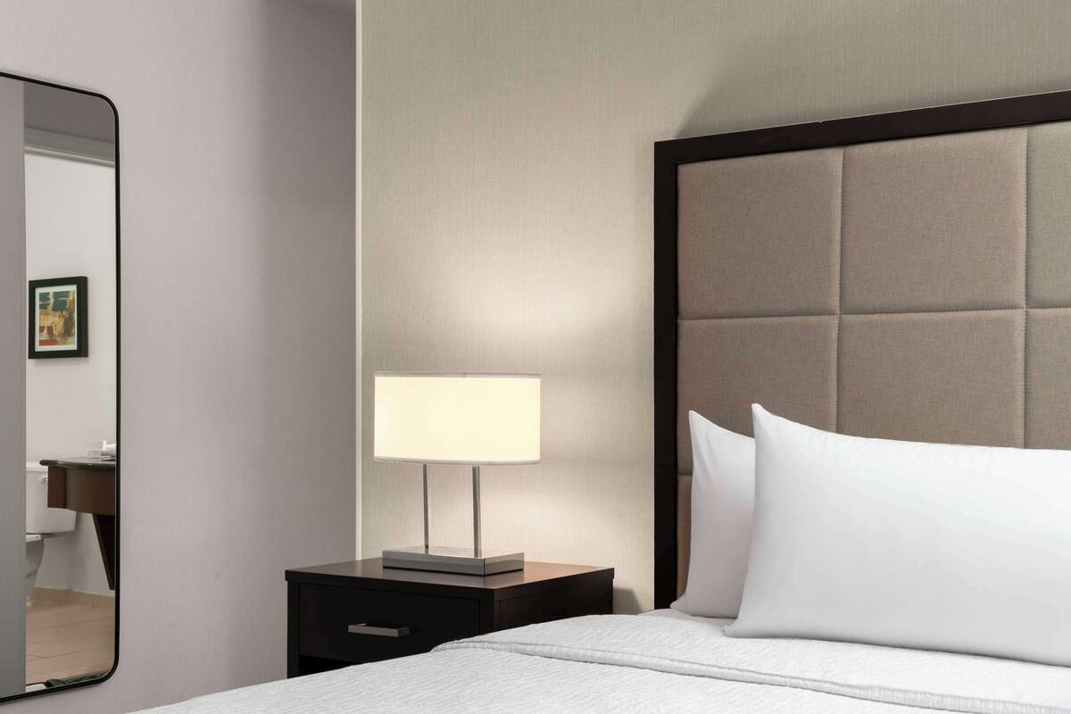Een hotelkamer met een bed, nachtkastje met lamp, spiegel en hoofdeinde.