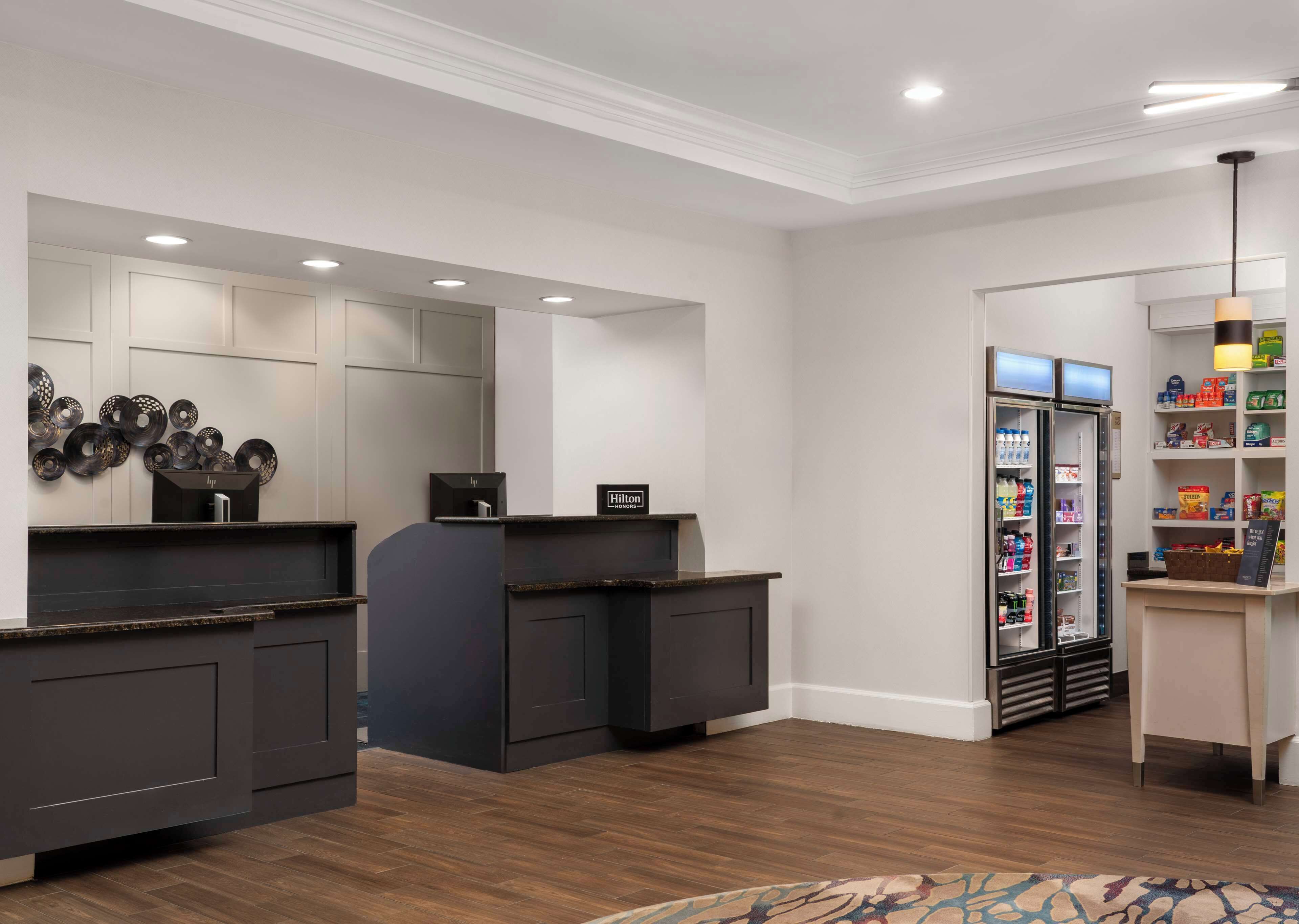 A hotel reception area with a modern design, including a counter, a minibar, and a refrigerator stocked with beverages.