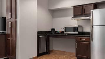Cocina compacta con armarios de madera oscura, un refrigerador de acero inoxidable, un microondas y un lavavajillas.