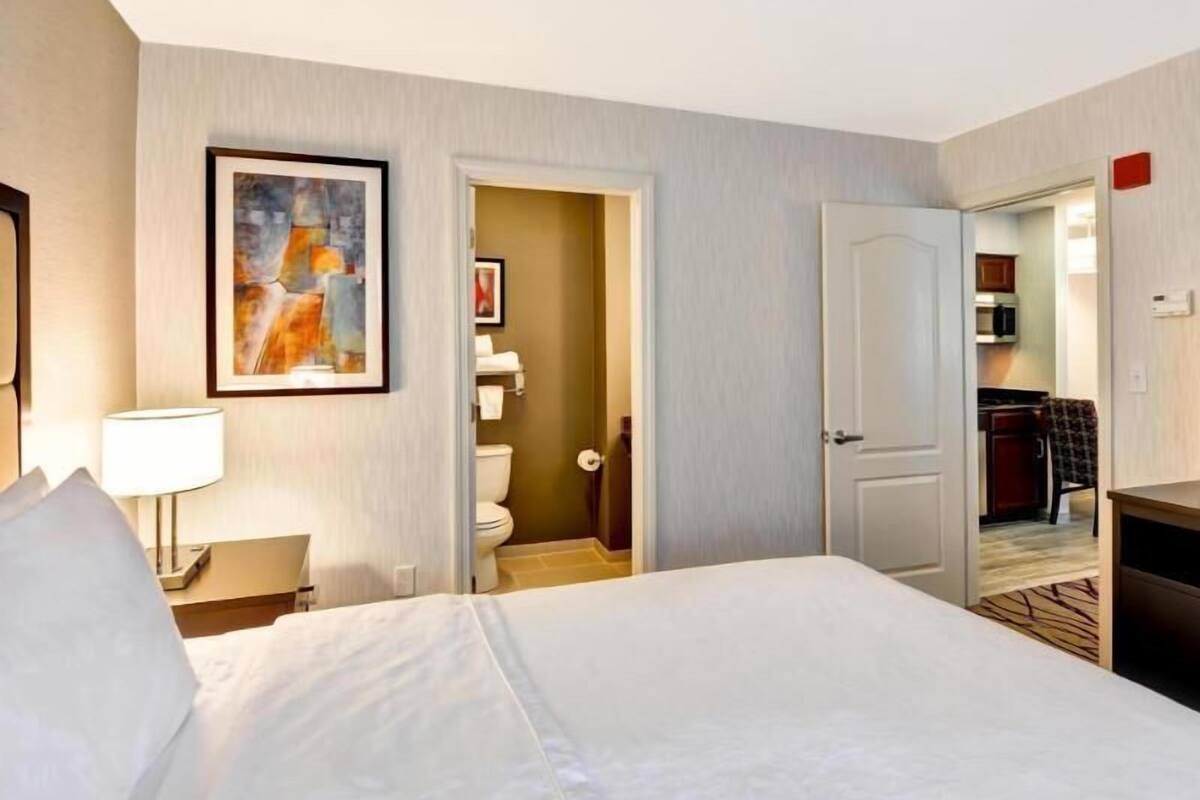 Een hotelkamer met een bed, een schilderij, een badkamer en een kitchenette.