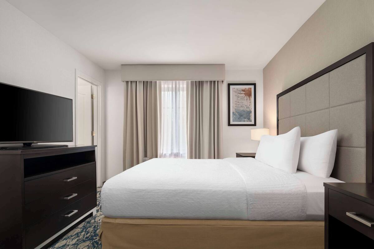 Een hotelkamer met een bed, een televisie, een bureau en een raam met gordijnen.