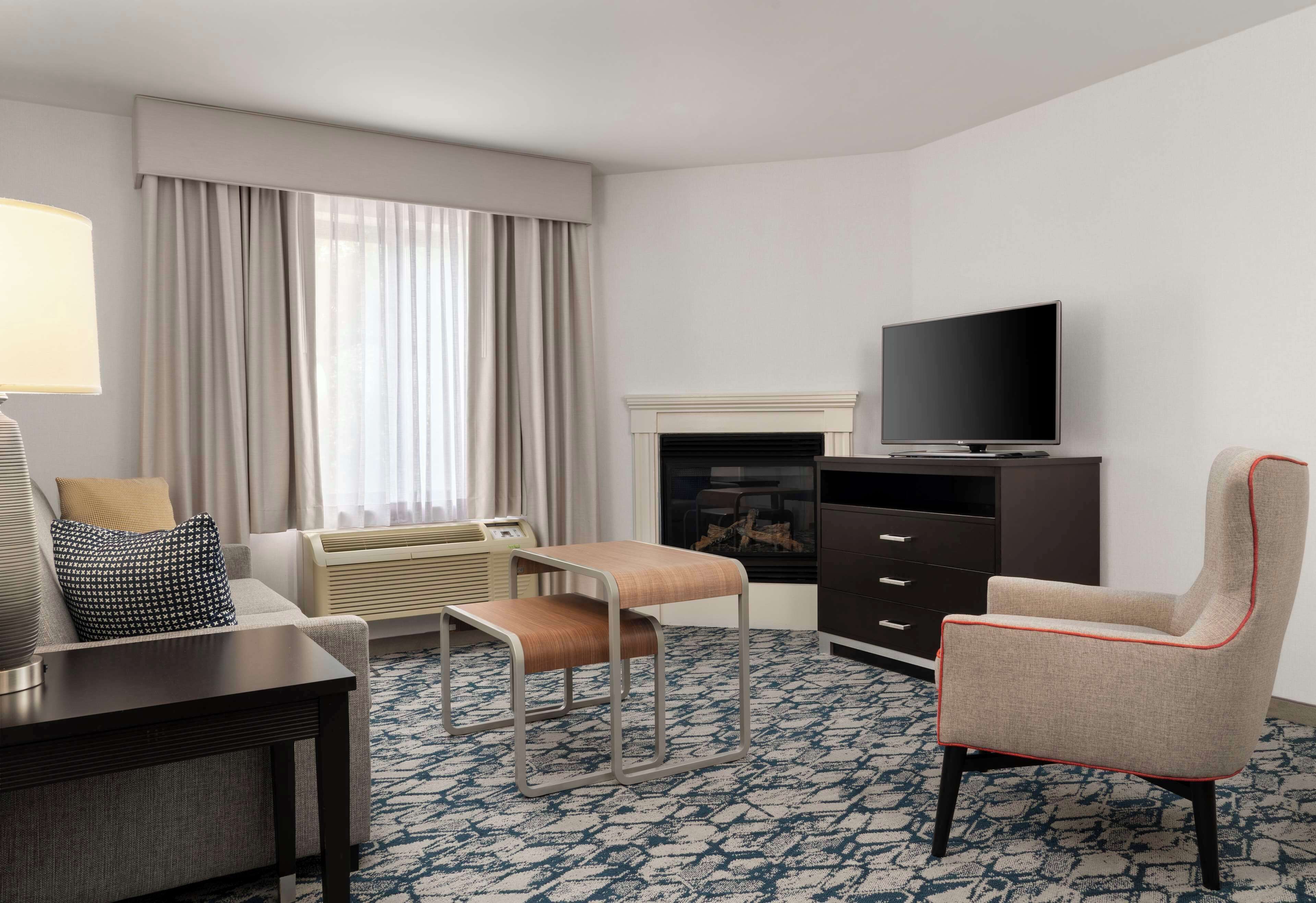 Une chambre d’hôtel avec un canapé, une petite table, une télévision, une cheminée et un fauteuil.