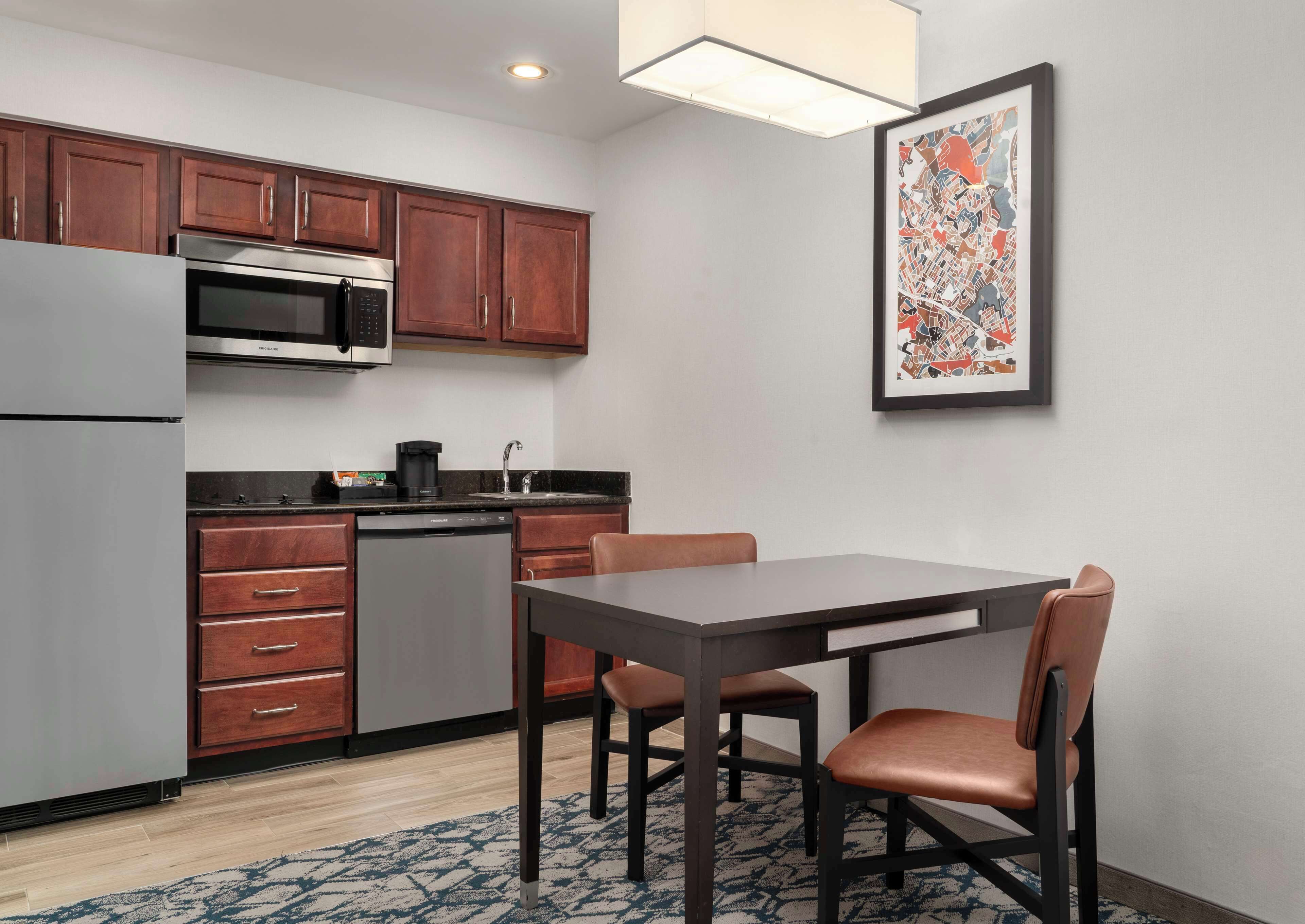 A compact kitchen with wooden cabinets, a built-in microwave, a dishwasher, and a dining table with chairs.