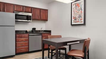A compact kitchen with wooden cabinets, a built-in microwave, a dishwasher, and a dining table with chairs.