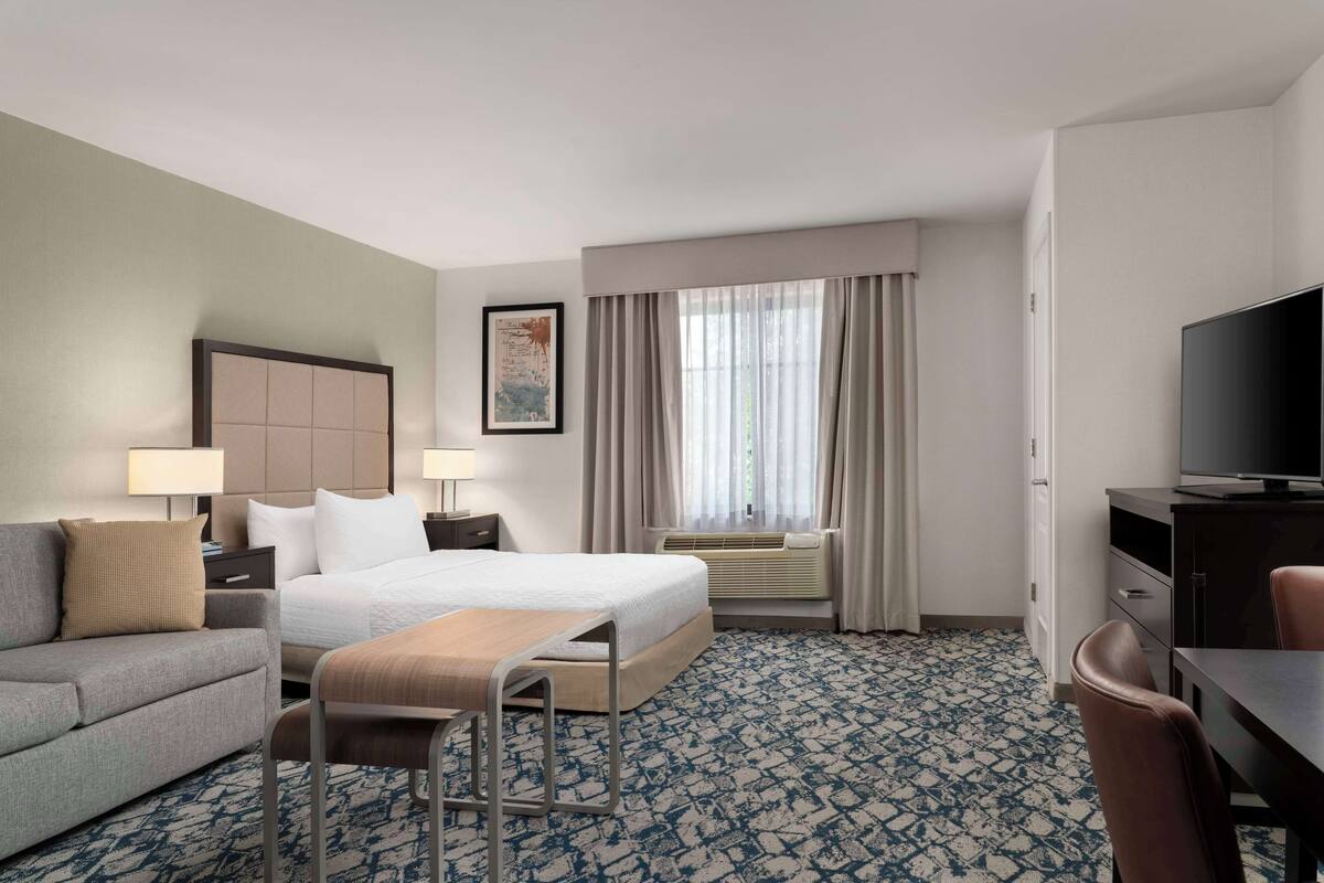Een hotelkamer met een bed, een bank, een bureau, een televisie en een raam met gordijnen.