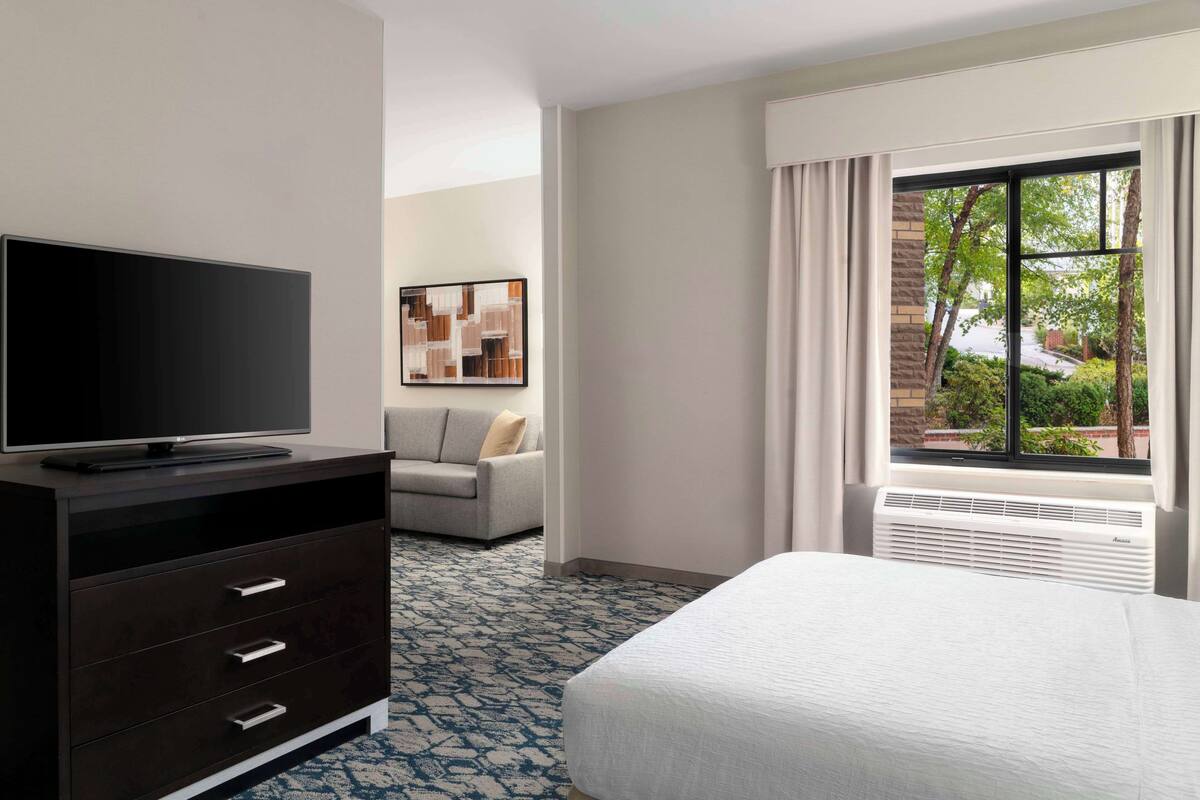 Hotelkamer met een bed, een televisie op een dressoir, een bank en een raam met uitzicht op groen.