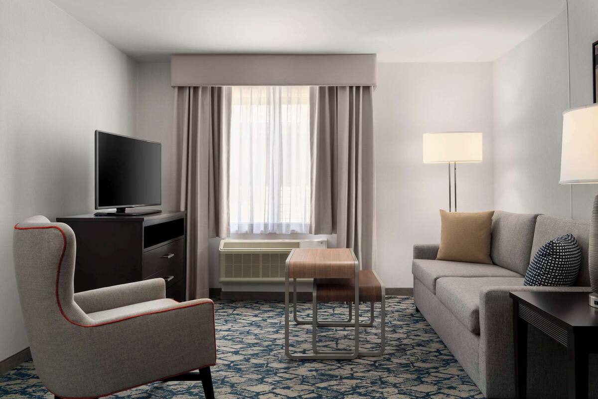 Een hotelkamer met een flatscreen televisie, een bank, een stoel, een bijzettafeltje en een lamp.