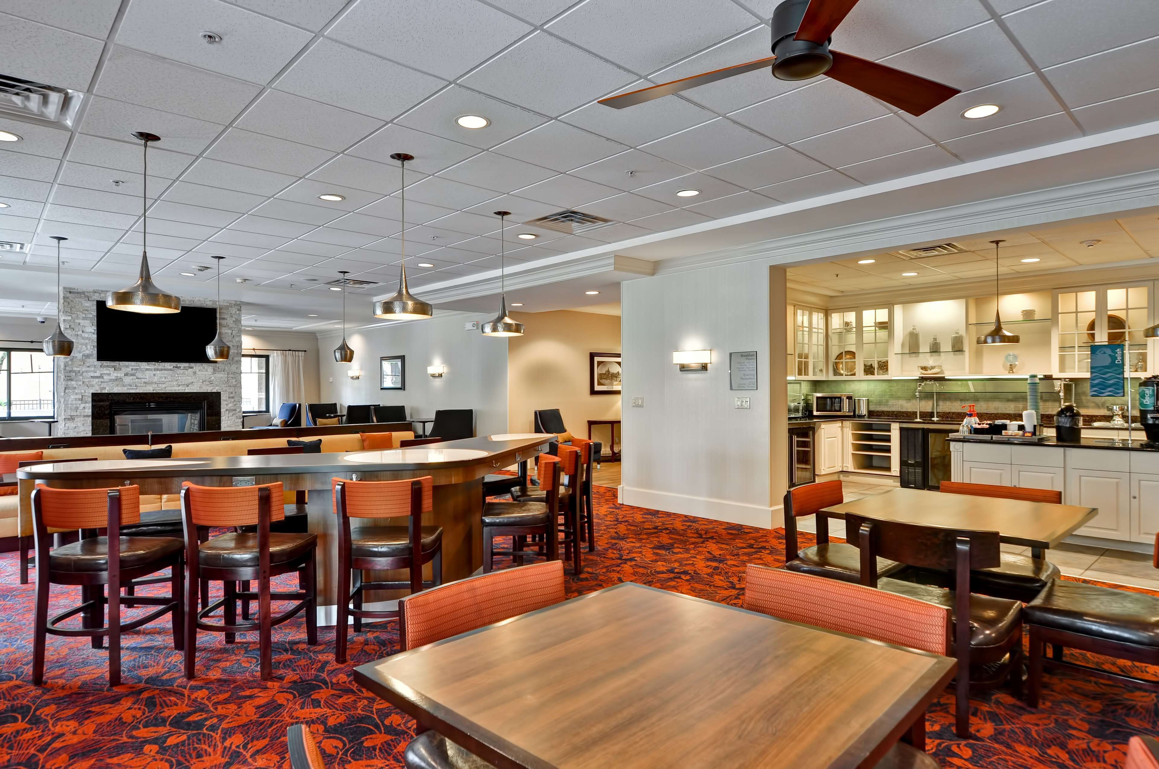 A hotel lobby with a central seating area, a kitchen in the background, and a ceiling fan.