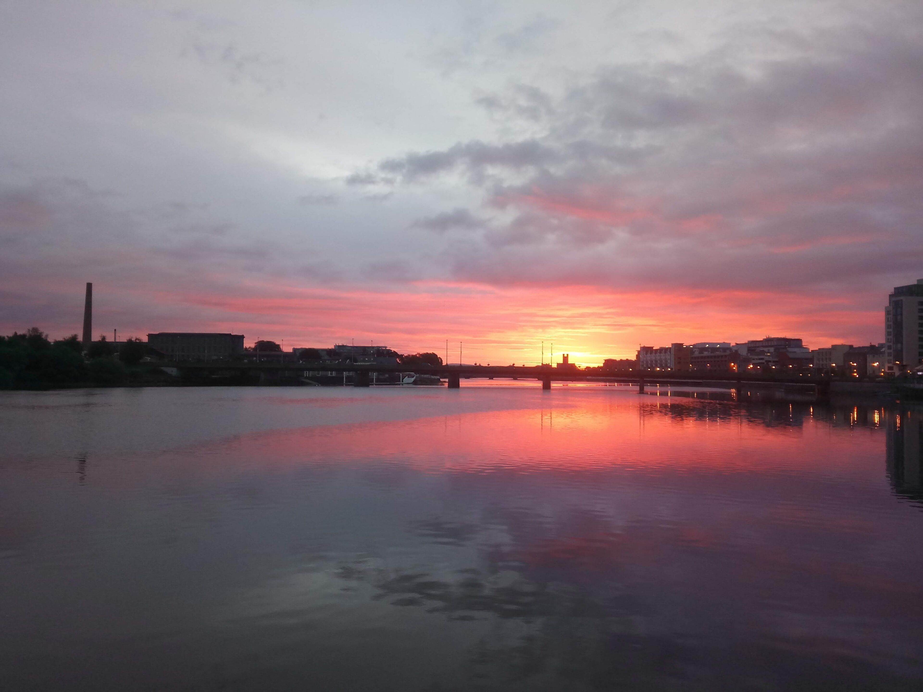 A sunset over a calm river with buildings on the opposite bank.