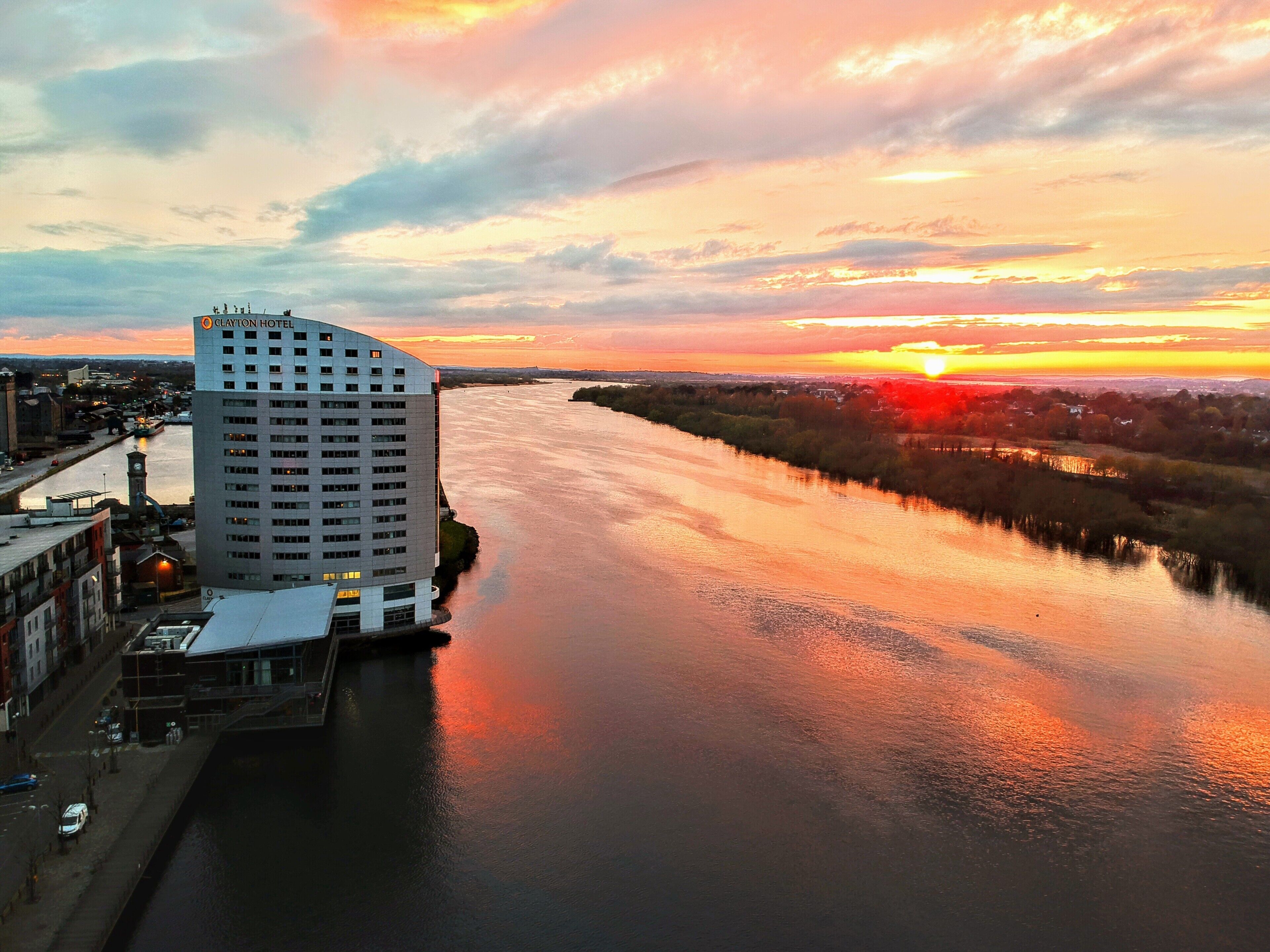 Un hotel moderno de gran altura, ubicado junto a un río con vistas al atardecer.