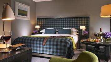 A hotel room with a bed, two bedside tables, a desk, a chair, and a small table with food and drinks.