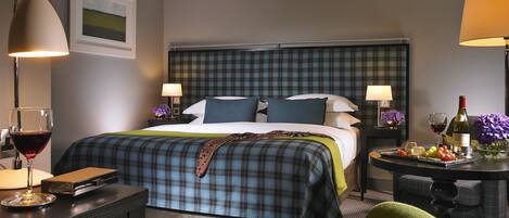 A hotel room with a bed, two bedside tables, a desk, a chair, and a small table with food and drinks.
