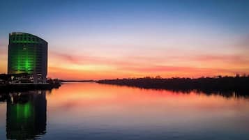 Un hôtel au design moderne, situé au bord d’une étendue d’eau paisible, dont les eaux reflètent le ciel au coucher du soleil.