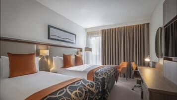 A hotel room with two beds, a desk, a chair, and a large window with curtains.