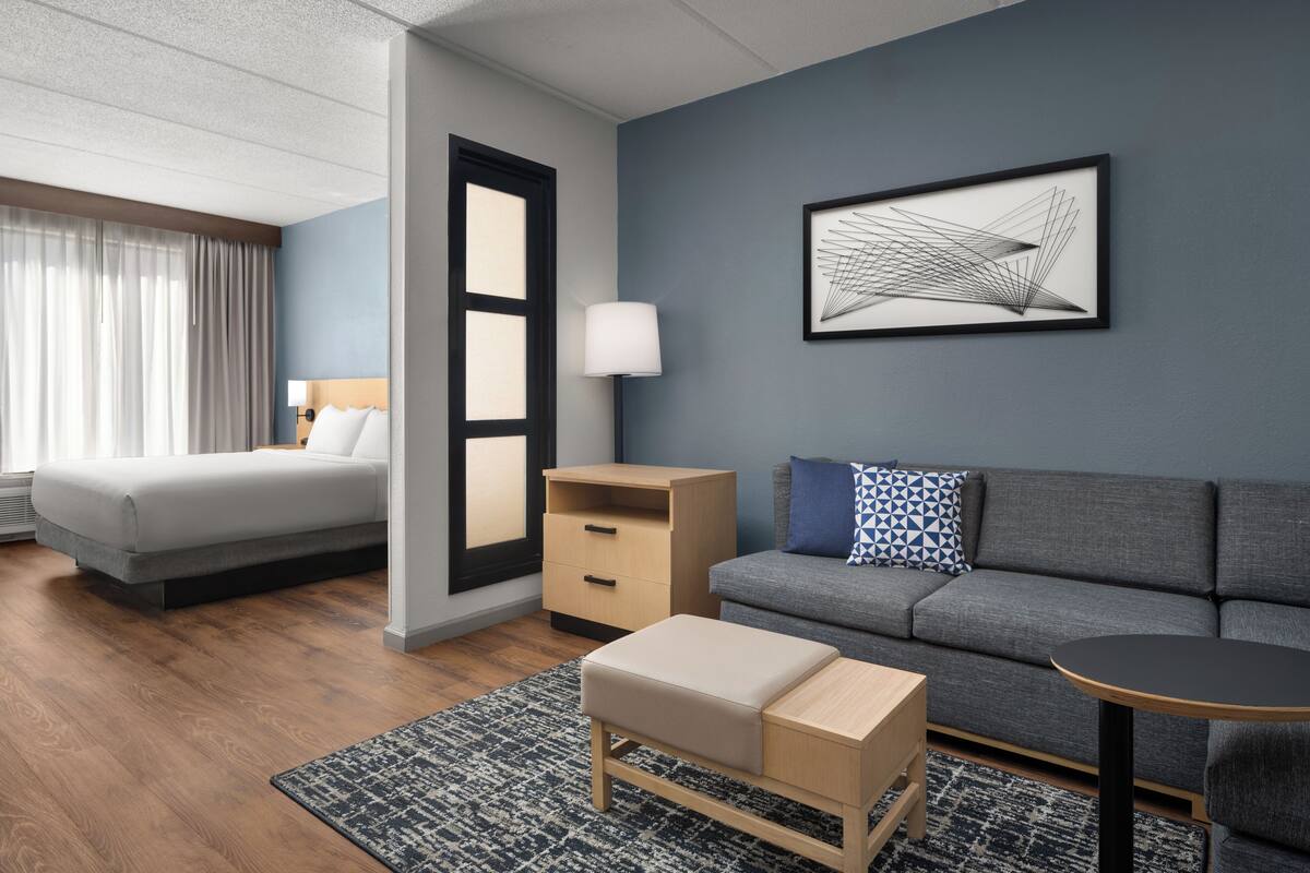 Ein modernes Hotelzimmer mit Bett, einer Couch, einem kleinen Tisch, einem Nachttisch und einer Wandlampe.