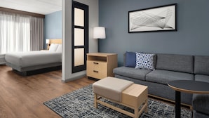 Ein modernes Hotelzimmer mit Bett, einer Couch, einem kleinen Tisch, einem Nachttisch und einer Wandlampe.