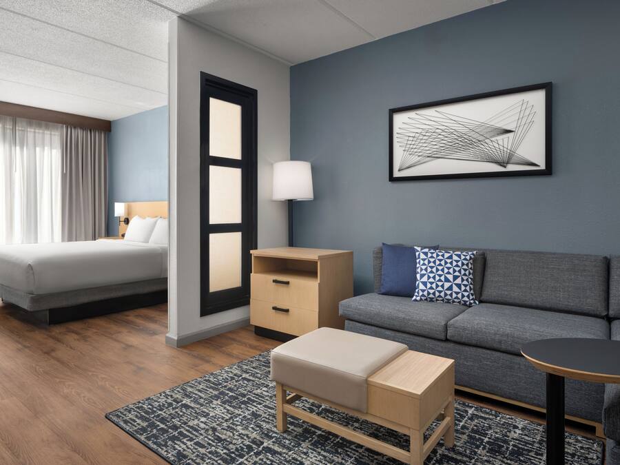A modern hotel room with a bed, a sofa, a small table, a nightstand, and a wall-mounted lamp.