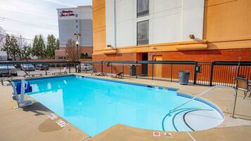 A swimming pool with a 3 FT depth sign, surrounded by a fence, and a Hampton Inn & Suites building in the background.