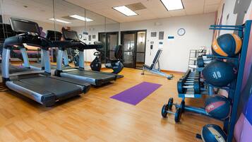 A gym with treadmills, ellipticals, and a weight rack with dumbbells and medicine balls.