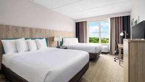A hotel room with two beds, a desk, a chair, a TV, and a window with a view of greenery.