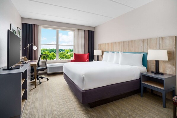 A hotel room with a large bed, a desk with a computer, a chair, and a TV.