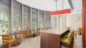 A modern dining area with a central island, wooden chairs, and large windows with blinds.