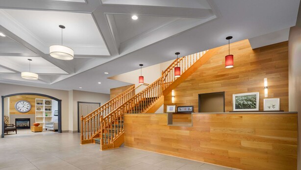A spacious lobby with a wooden staircase, a reception desk, and a large wall clock.