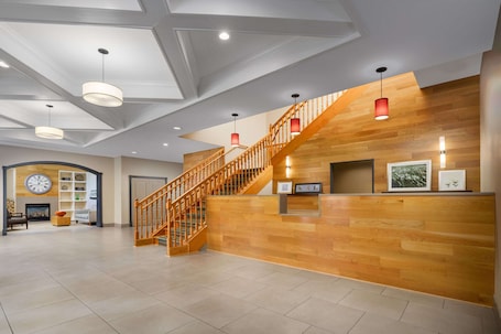 A spacious lobby with a wooden staircase, a reception desk, and a large wall clock.
