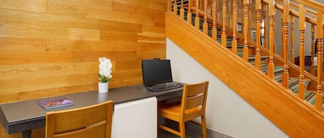 A wooden floor, a desk with a laptop, a chair, a small white cabinet, and a staircase with wooden railings.