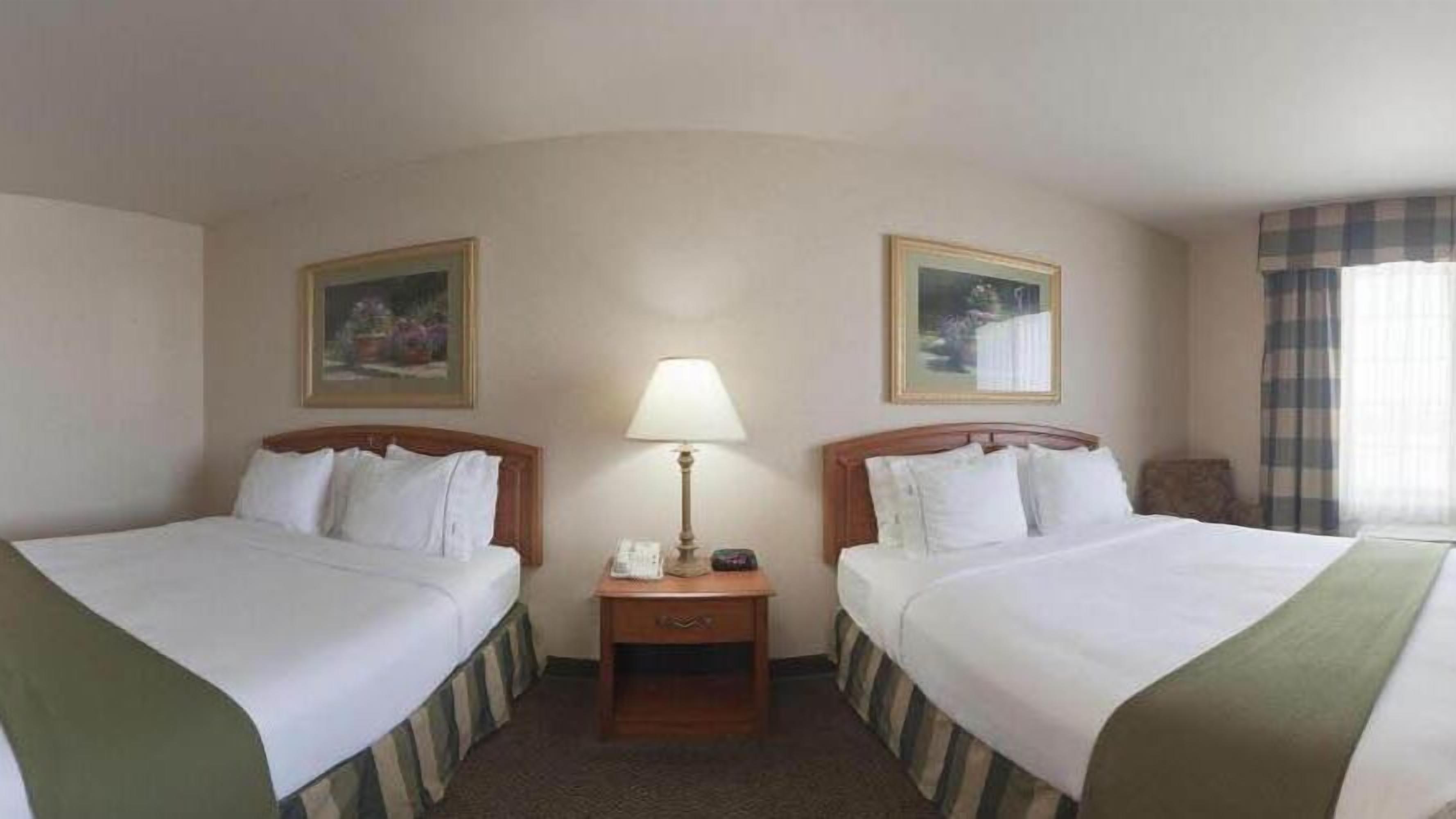 Une chambre d’hôtel avec deux lits, une table de chevet avec une lampe et deux tableaux encadrés accrochés aux murs.