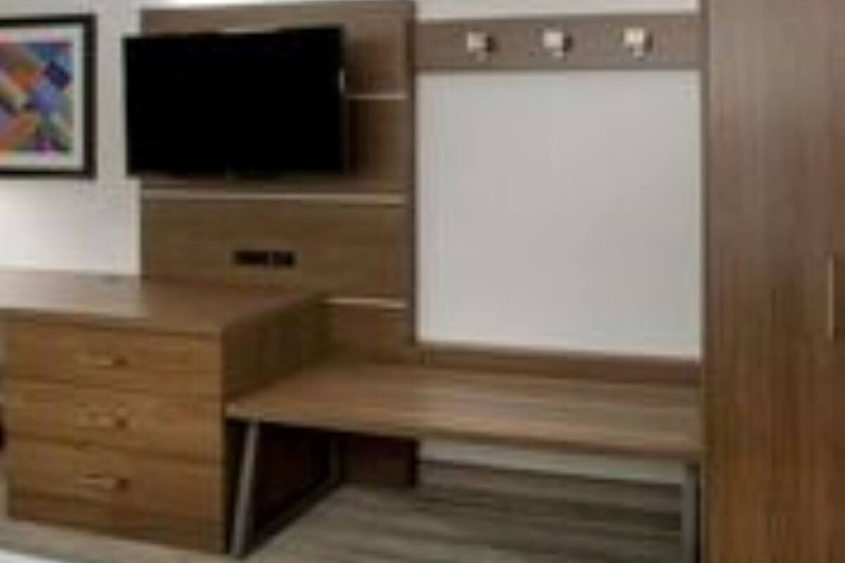 Una habitación de hotel moderna con un escritorio de madera, un televisor de pantalla plana, un armario y una cama.