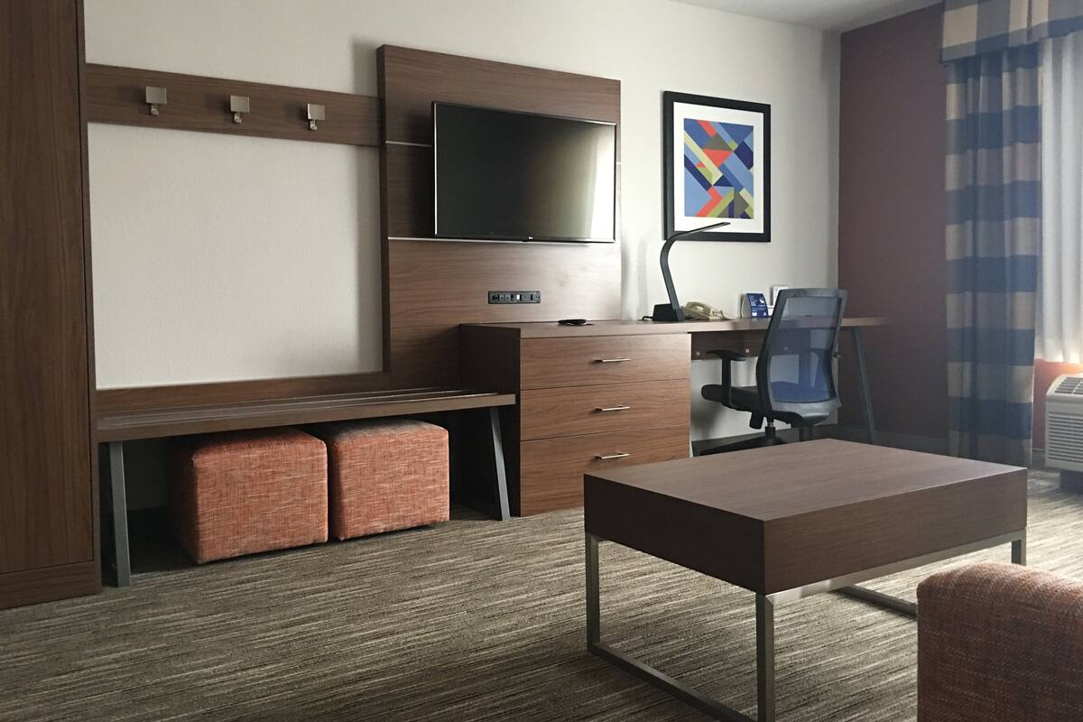 Habitación de hotel con cama, escritorio, silla, televisor y un cuadro en la pared.