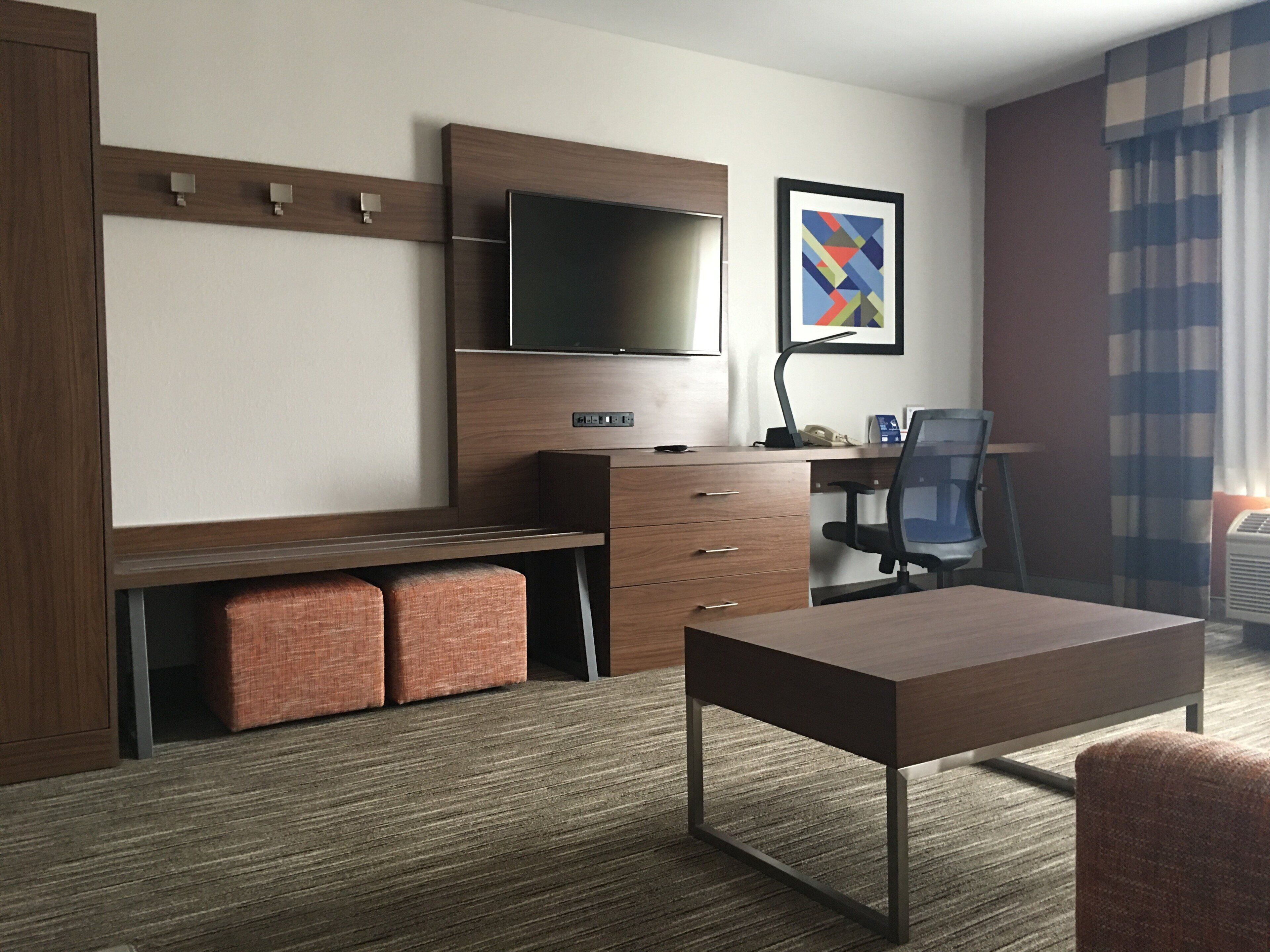 Une chambre d’hôtel avec un lit, un bureau et une chaise, une télévision et un tableau encadré au mur.