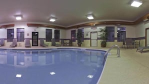 An indoor swimming pool with lounge chairs and a small table, surrounded by walls with doors and windows. - Holiday Inn Express Greensburg by IHG (Greensburg)