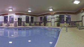An indoor swimming pool with lounge chairs and a small table, surrounded by walls with doors and windows. - Holiday Inn Express Greensburg by IHG (Greensburg)