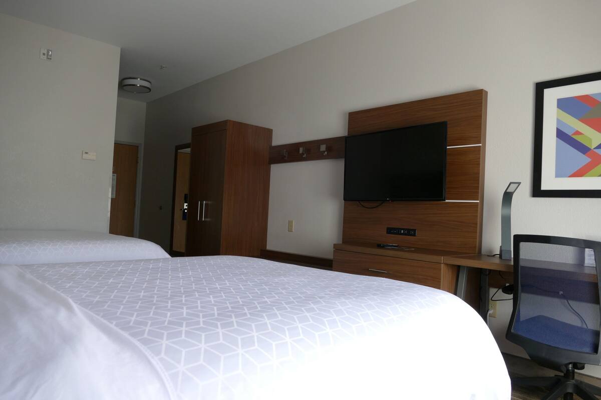 Una habitación de hotel con dos camas, televisión, escritorio con silla y armario.
