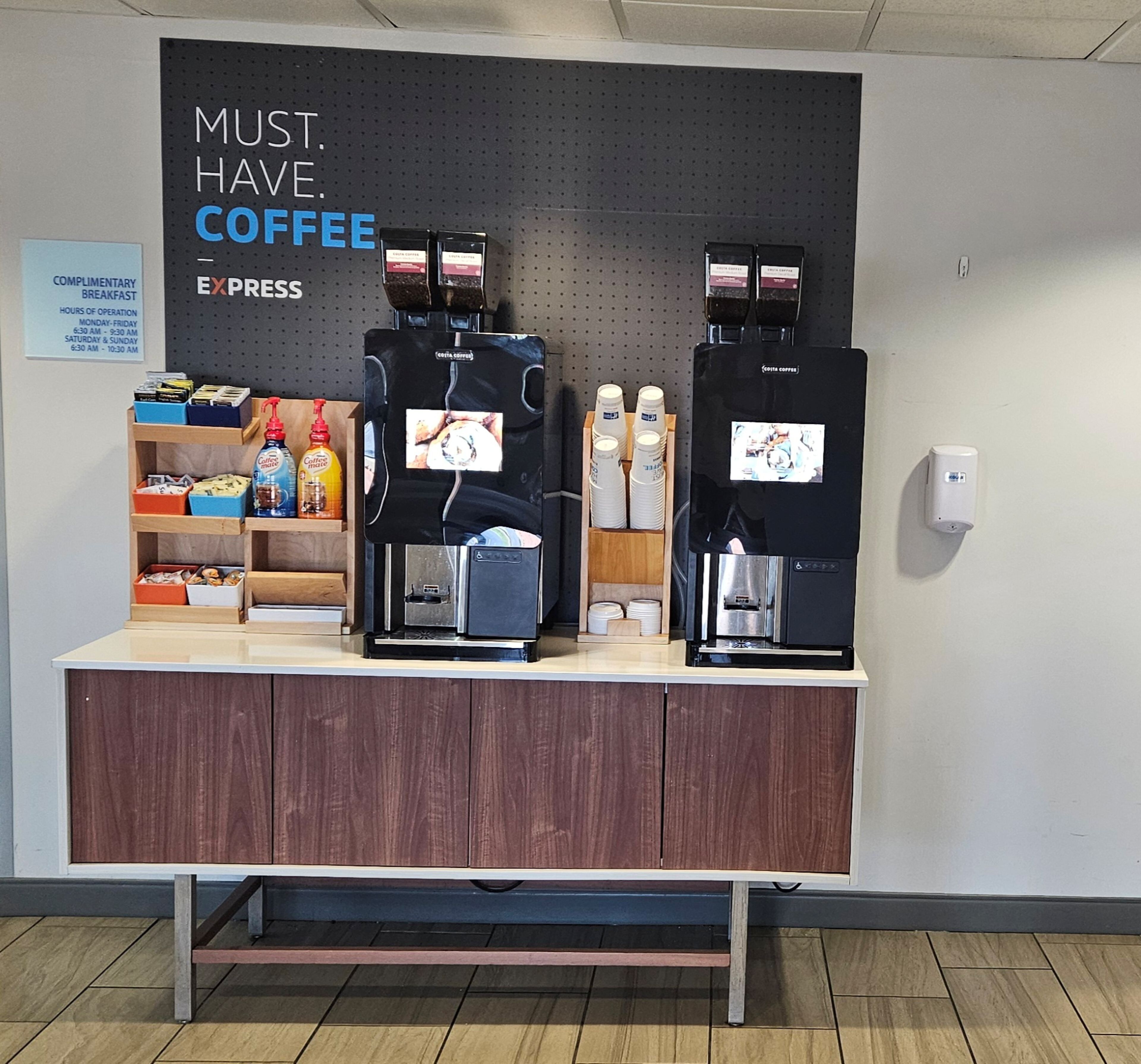 Una estación de café con dos máquinas de espresso, un cartel que dice 'MUST HAVE COFFEE EXPRESS' y varios artículos relacionados con el café en estantes.