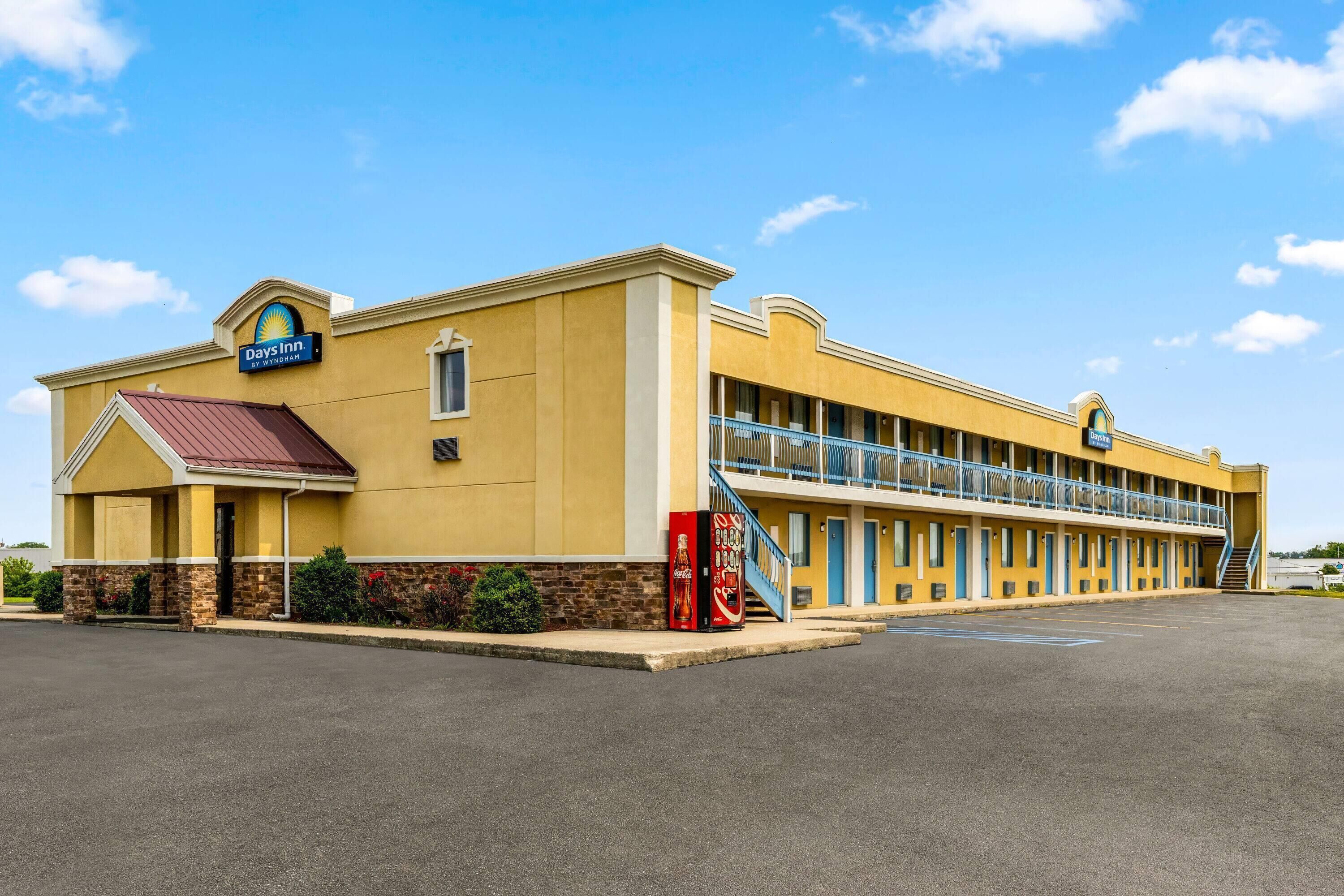 A Days Inn building with a yellow facade, a red awning, and a Coca-Cola vending machine.