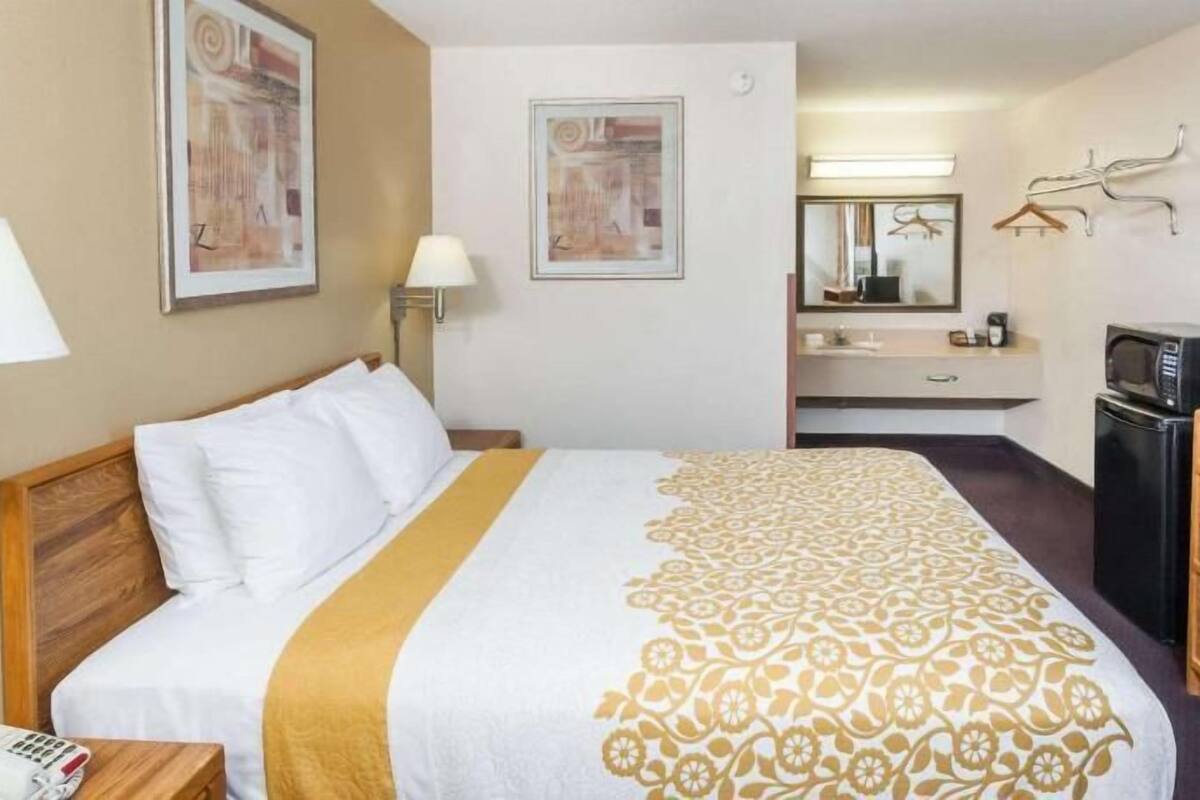 Hotellihuone, jossa on sänky, työpöytä puhelimineen, televisio, jääkaappi, peili sekä kylpyhuone, jossa on pesuallas ja pyyheteline.