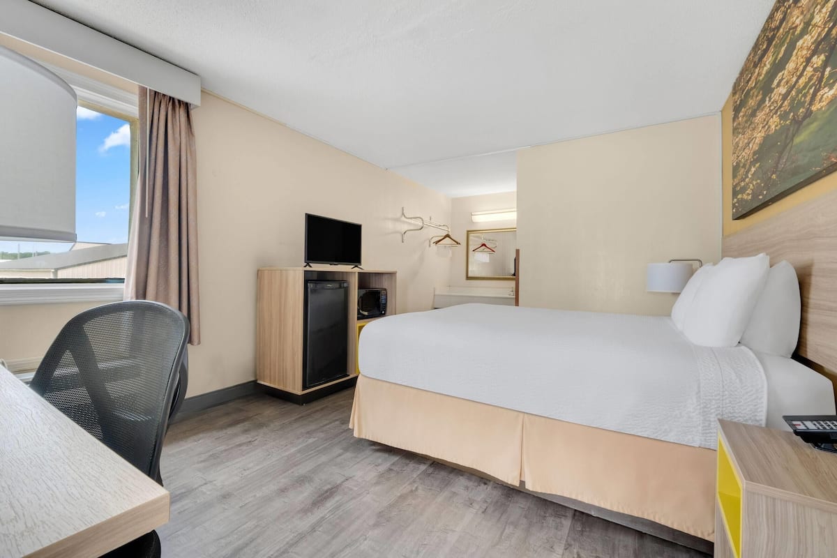 Hotellihuone, jossa on sänky, työpöytä, tuoli, televisio ja pieni jääkaappi.