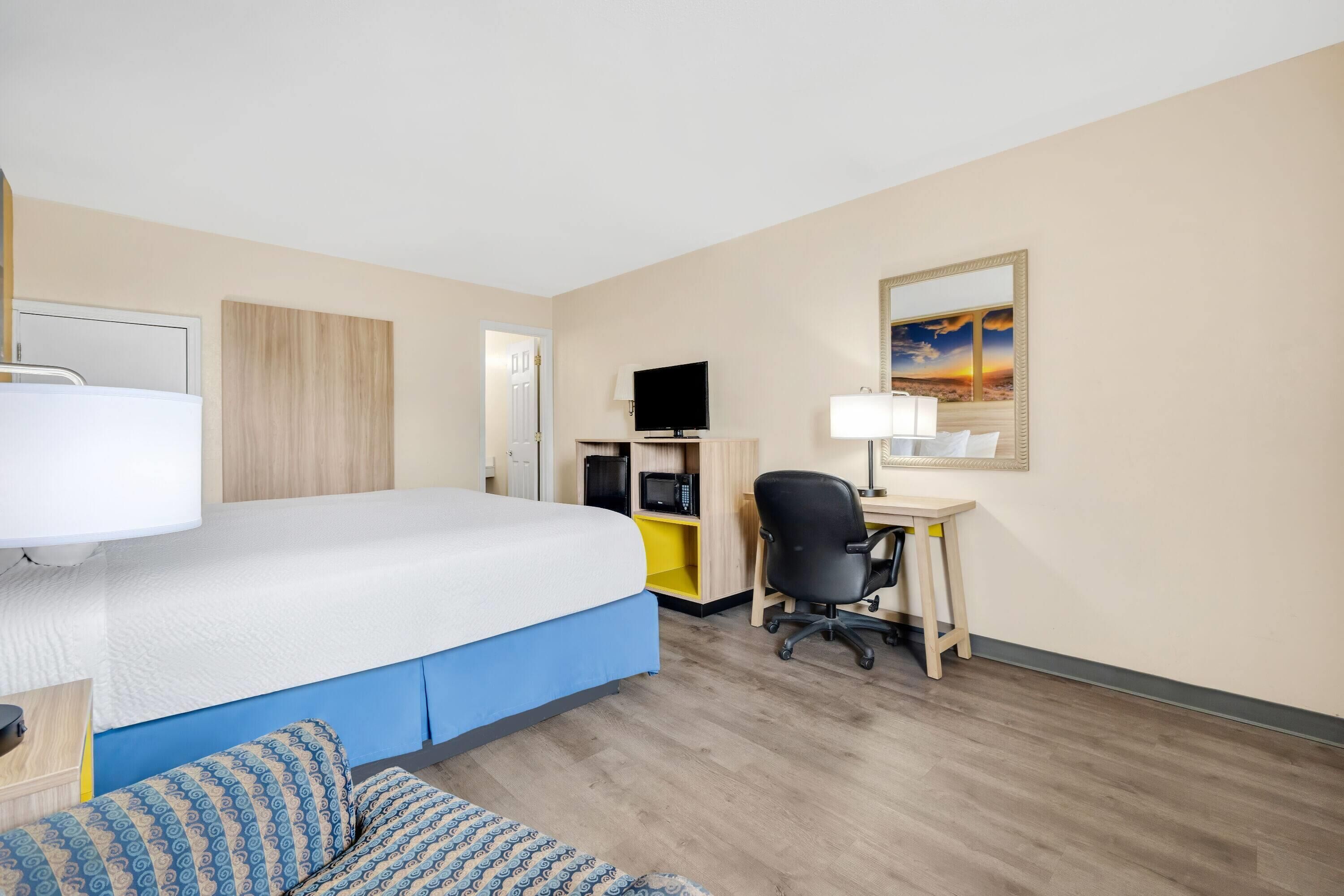 Camera d'albergo con letto, scrivania, sedia, televisore e un quadro appeso al muro.