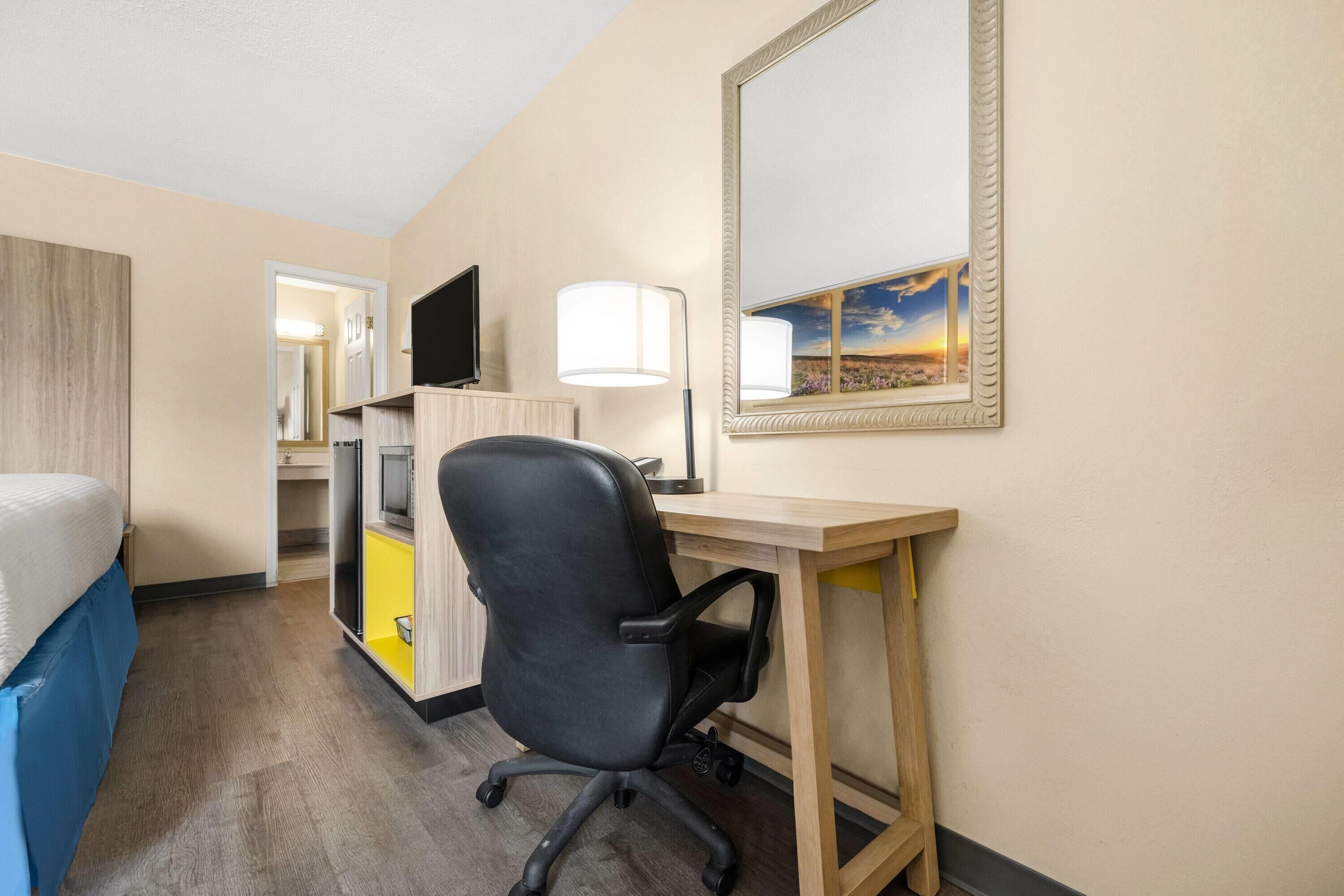 A hotel room with a bed, a desk with a chair, a TV, a lamp, and a painting on the wall.